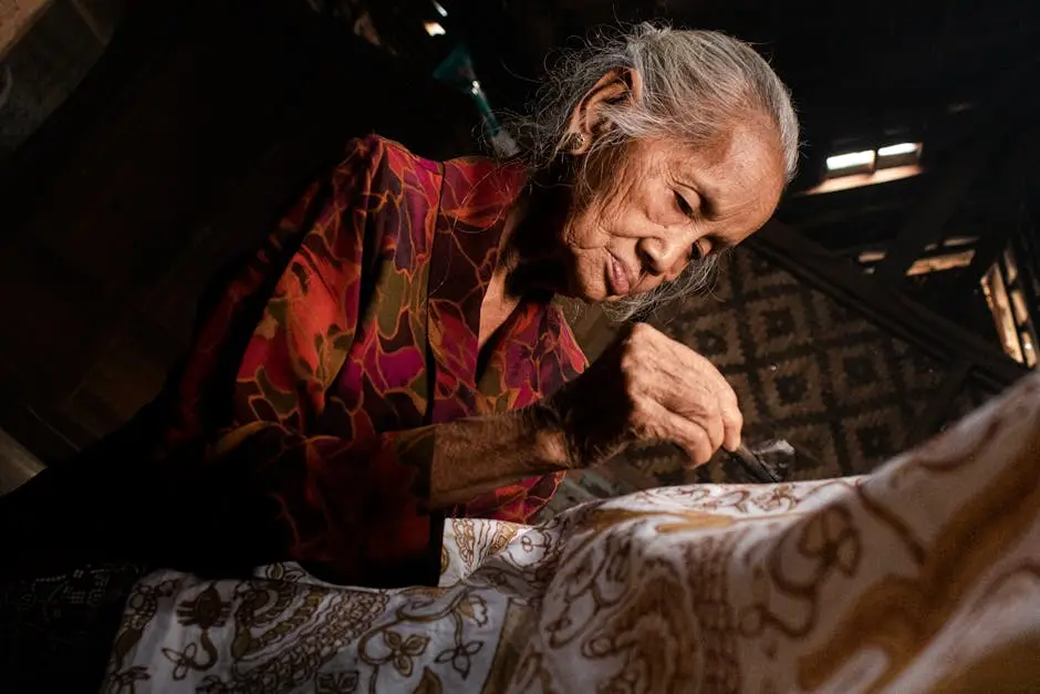 Proses pembuatan batik tulis yang detail, menampilkan tangan seorang pengrajin yang sedang mengaplikasikan malam pada kain.