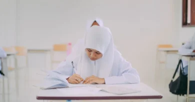 Seorang wanita muda Indonesia belajar bahasa Inggris otodidak di laptop dengan buku dan catatan di meja.