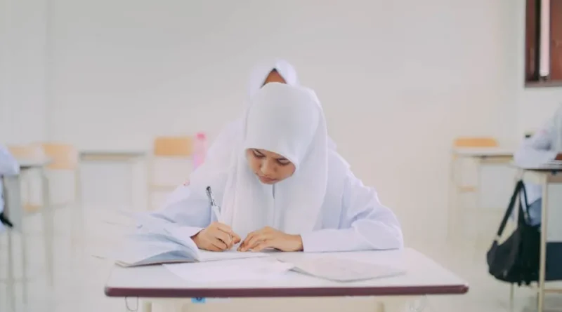 Seorang wanita muda Indonesia belajar bahasa Inggris otodidak di laptop dengan buku dan catatan di meja.